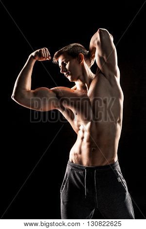 Strong bodybuilder man posing with perfect abs, houlders, biceps, triceps and chest on black background.