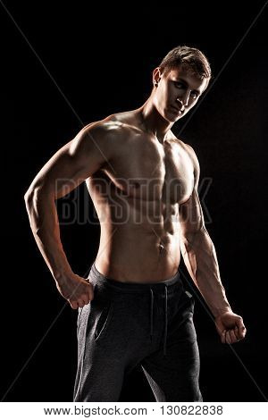 Strong bodybuilder man posing with perfect abs, houlders, biceps, triceps and chest on black background.