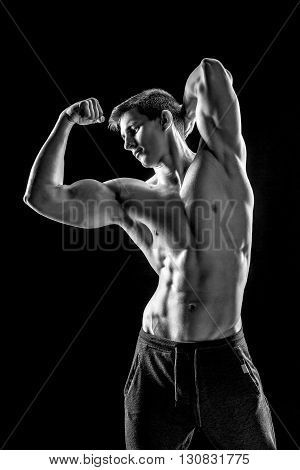 Strong bodybuilder man posing with perfect abs, houlders, biceps, triceps and chest on black background. Black and white
