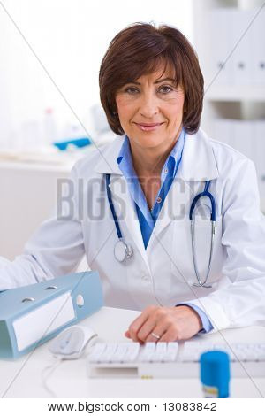 Senior femmina medico seduto alla scrivania lavorando presso offiice.