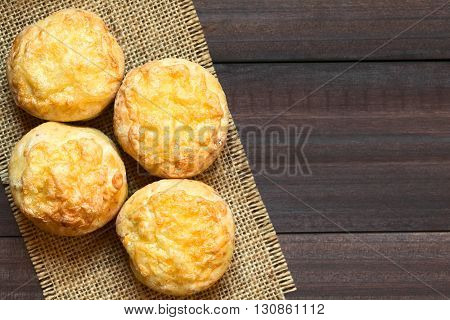 Hungarian traditional Cheese Pogacsa savory baked bread-like pastry photographed overhead on dark wood with natural light (Selective Focus Focus on the top of the pastries)