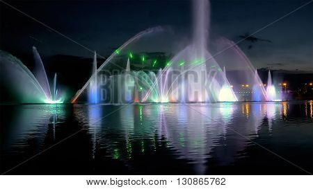 Amazing fantastic colorful fountain with bright illumination on the water pond or river with beautiful reflection at the evening or night. Beauty urban recreational concept.
