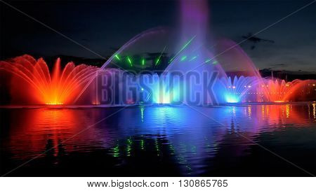Amazing fantastic colorful fountain with bright illumination on the water pond or river with beautiful reflection at the evening or night. Beauty urban recreational concept.