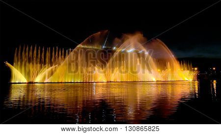 Amazing fantastic colorful fountain with bright illumination on the water pond or river with beautiful reflection at the evening or night. Beauty urban recreational concept.