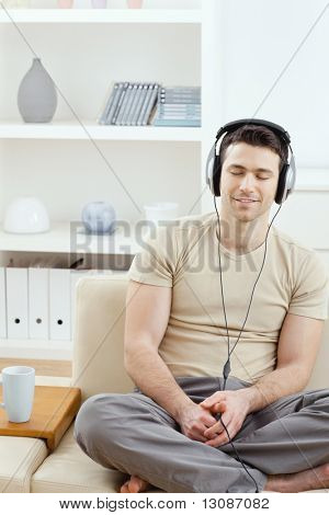 Casual uomo ascolto musica con le cuffie a casa, rilassante con gli occhi chiusi, sorridente.
