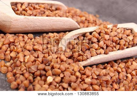 Heap of uncooked brown buckwheat groats with wooden spoon lying on structure of concrete concept for healthy eating and nutrition