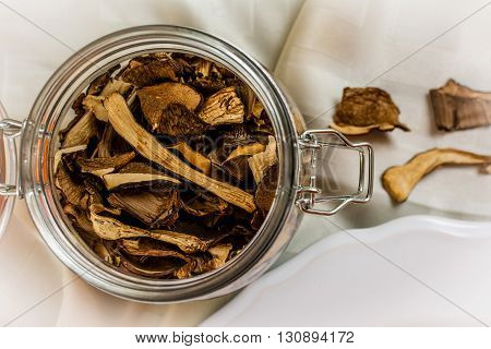 Dry mushrooms in glass bottle on white cloth