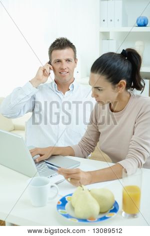 Mladý pár sedící u stolu, nakupování na internetu z domova. Volání telefon, pomocí laptopcomputer a
