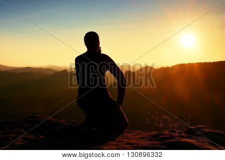 Sportsmann Hiker In Black Sportswear Sit On Mountain Top And Take A Rest. Tourist  Watch Down To Mor