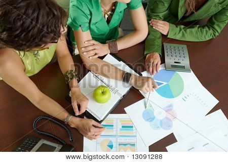 Unge erhvervskvinder sidder ved bord i mødelokalet, diskuterer finacial diagrammer. Overhead skud.