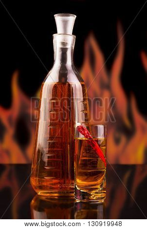 Bottle and a glass of vodka with red chili pepper on the background of flames.