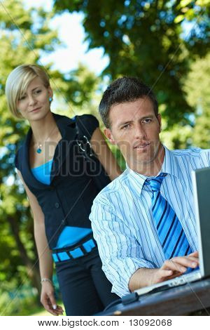 Casual uomo d'affari utilizzando laptopn nel periodo estivo Parco, giovane donna guarda da dietro.