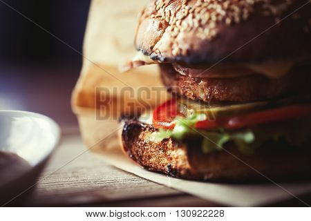 Delicious burger with pork steak tomato cucumber and fresh salad grilled and put between two bagels with sesame seeds. Unhealthy but so tasty fast food. Close up photo in macro mode