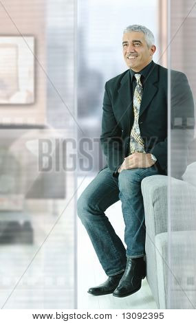 Casual businessman sitting on couch in modern office, smiling.