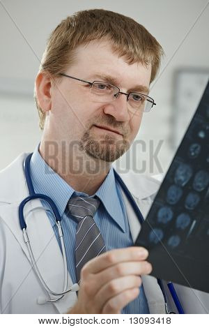 V ordinaci - portrét středního věku mužského lékaře při pohledu na tomograf prohledávání počítače.