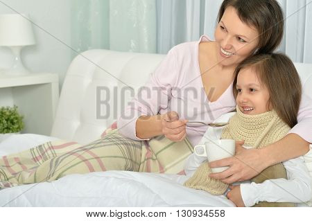 Sick little girl with mother in bed with hot drink at home