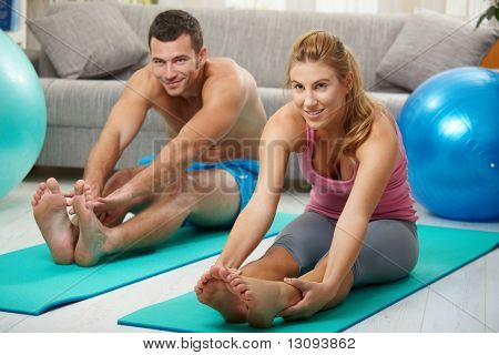 Mladý pár sedící na fitness matrace a streching nohy před treining