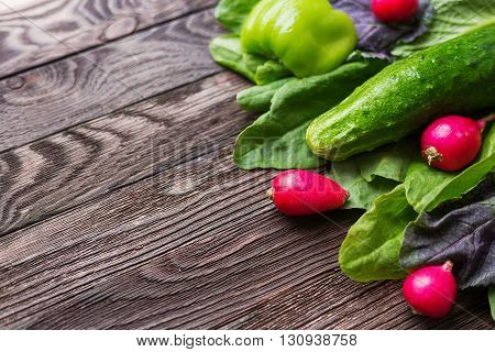 Fresh ingredients for salad - sorrel leaves radishes cucumber sweet pepper on wooden background. Rustic table with tasty vegetables. Place for text.