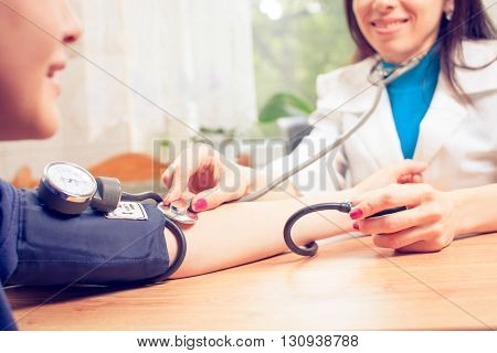 Beautiful young female doctor is checking the blood pressure of the patient.