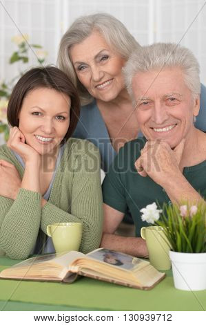 Cute family portrait , adult daughter with senior parents drinkig tea