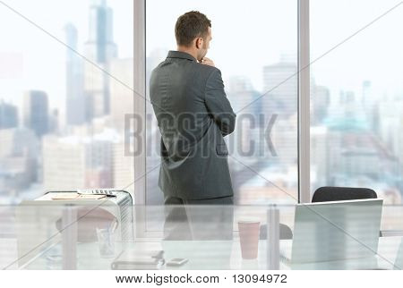 Forretningsmand tænker i office, ser ud af vinduerne til downtown vista.