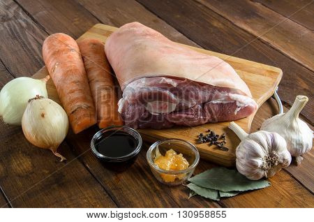 Raw pork knuckle with onion, carrot, garlic, cloves, honey, soy sauce on wooden table