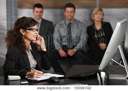 Businesswoman หนุ่มที่นั่งอยู่ที่โต๊ะในสำนักงาน recepcion พูดคุยในโทรศัพท์มือถือ ยิ้ม คนหว้า