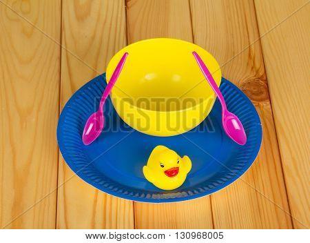 Colored plastic ware and rubber duck on a background of light wood.