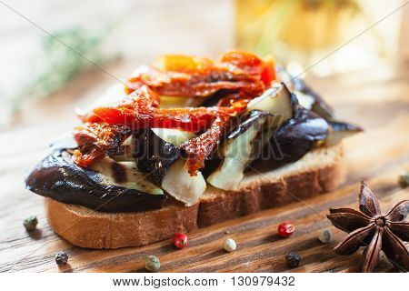 Vegetarian sandwich with sun-dried tomatoes and eggplant on wooden table. Front view. Closeup of bruschetta with grilled eggplant and sun-dried tomatoes on wooden background witn spices
