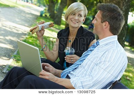 Giovani imprenditori seduto sulla panchina nel parco avendo luch e guardando il computer portatile.