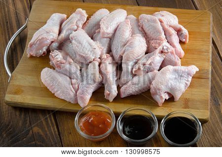raw chicken wings with sauces on wooden table
