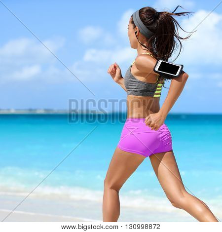 Fit woman running working out cardio exercise on summer tropical beach. Unrecognizable athlete runner jogging intense wearing phone armband holder for music motivation listening on smartphone app.