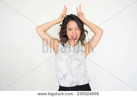 Portrait Of Playful Young Asian Woman Wearing Blouse Grimacing And Showing Horns. Childishness Conce