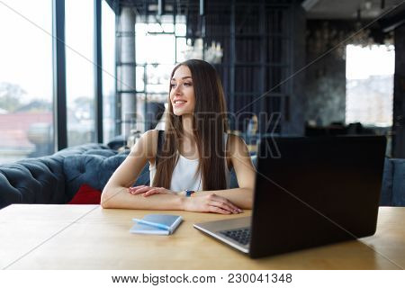 Young Woman Working On Her Laptop In The Restaurant. Girl Looking Out The Window.