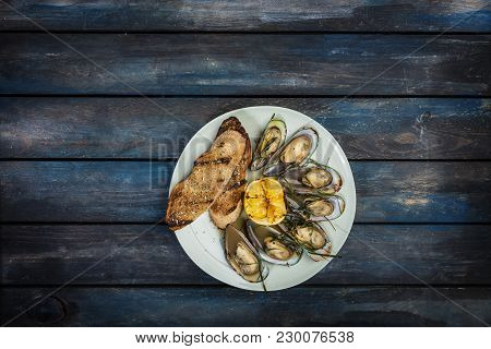 Mussels And Bread Toasts On On A White Plate. Served With Half Grilled Lemon. Wooden Background. Top