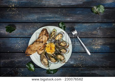 Mussels And Bread Toasts On On A White Plate. Served With Half Grilled Lemon, Fork And Leaves Of Kaf