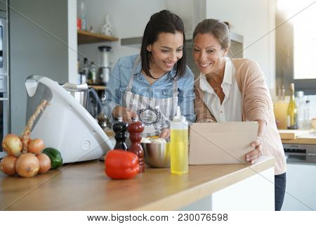 Friends cooking together with kitchen robot and tablet