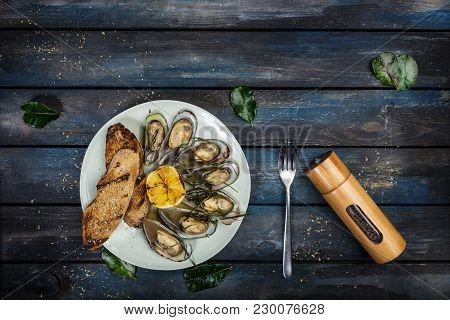 Mussels And Bread Toasts On On A White Plate. Served With Half Grilled Lemon, Fork And Leaves Of Kaf