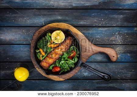 Grilled Salmon Fillet In A Frying Pan, Vegetables, Arugula With A Lemon. On The Cutting Board And Wo