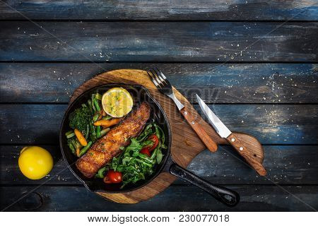 Grilled Salmon Fillet In A Frying Pan, Vegetables, Arugula With A Lemon Served With Cutlery. On The 