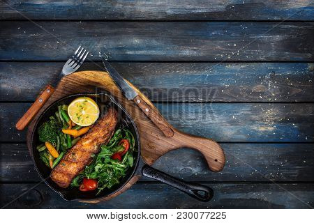 Grilled Salmon Fillet In A Frying Pan, Vegetables, Arugula With A Lemon Served With Cutlery. On The 