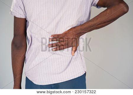 Close-up View Of A Young Man With Pain In Kidneys On Gray Background. Young Man With Back Ache Clasp