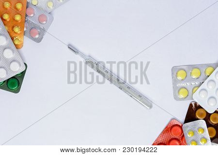 Photometer Of A Thermometer On A White Background Among Tablets Of Different Colors In Packages Of 2