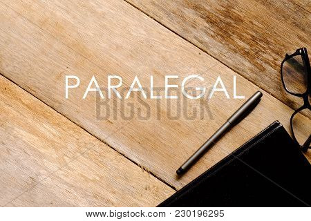 Top View Of Eyeglasses,notebook And Pen On Wooden Background Written With Paralegal.