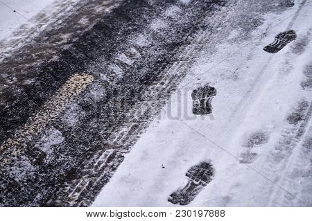 Car Tracks And Shoe Footprints In Snow On Icy Winter Asphalt Road.