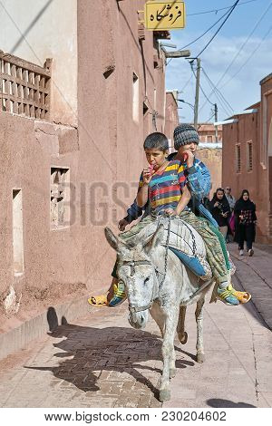 Abyaneh, Iran - April 26, 2017: Two Iranian Boys Ride On A Donkey Through A Narrow Street In The Tra