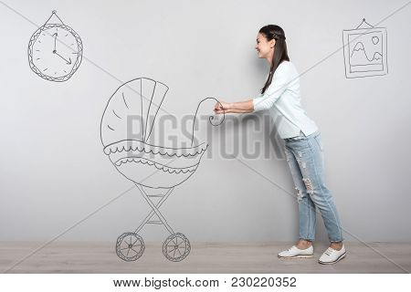 Loving Mother. Kind Responsible Young Woman Feeling Happy While Pushing An Imaginary Baby Carriage A