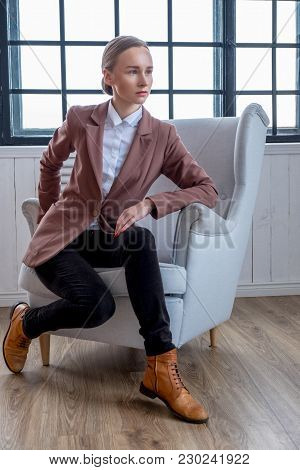 Casual Young Woman In A Brown Jacket Relaxing In A Room With Wondow.
