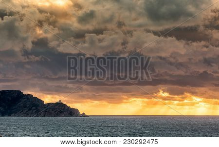 Evening Sun Rays Bursting Through Dark Stormy Clouds Onto The Mediterranean Sea Behind The Revellata