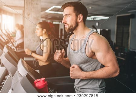 Close Up Of Two Well-built People That Run On The Running Machine. They Are Exerecising Very Hard. C